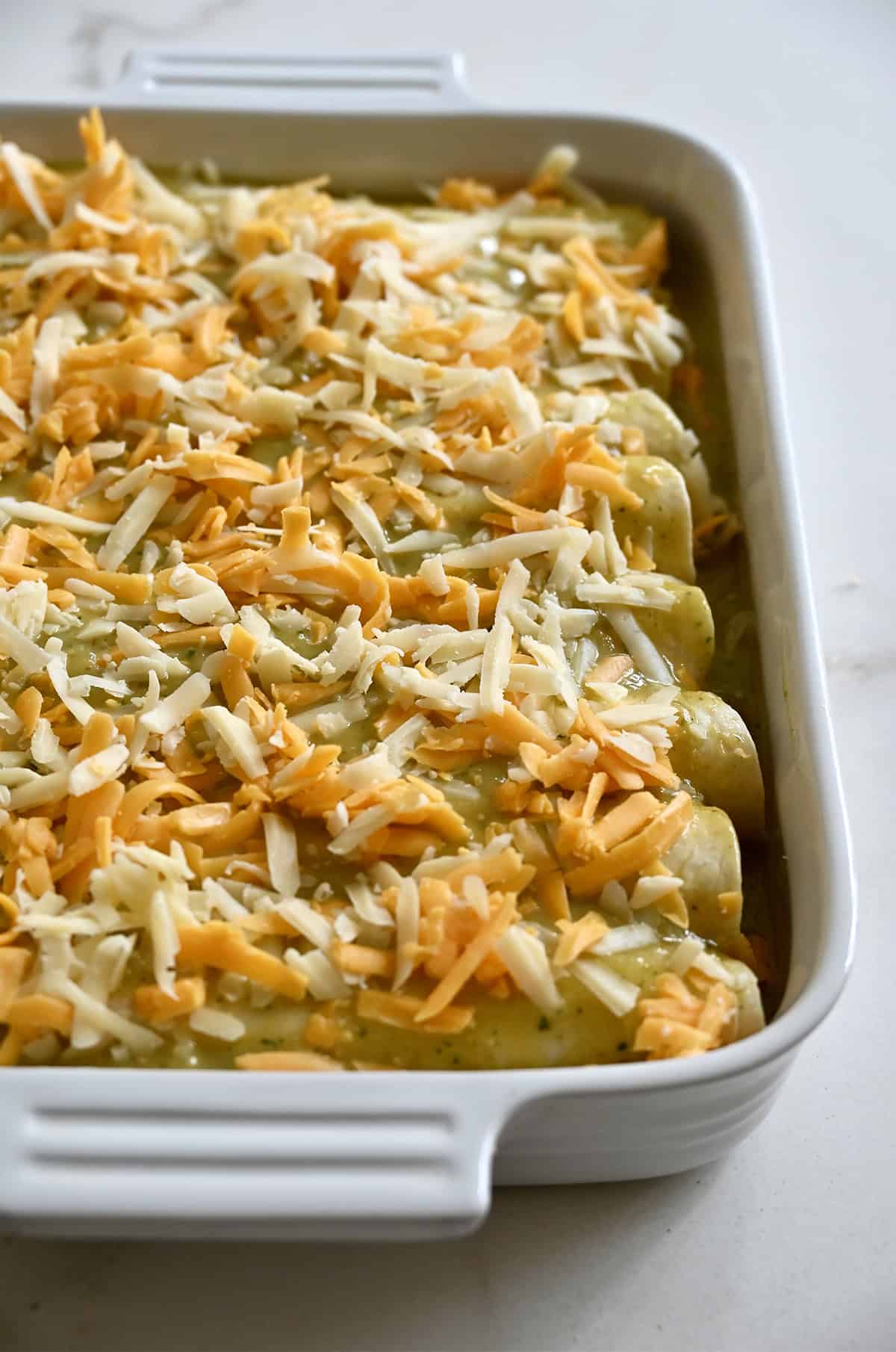Unbaked enchiladas topped with shredded cheese.