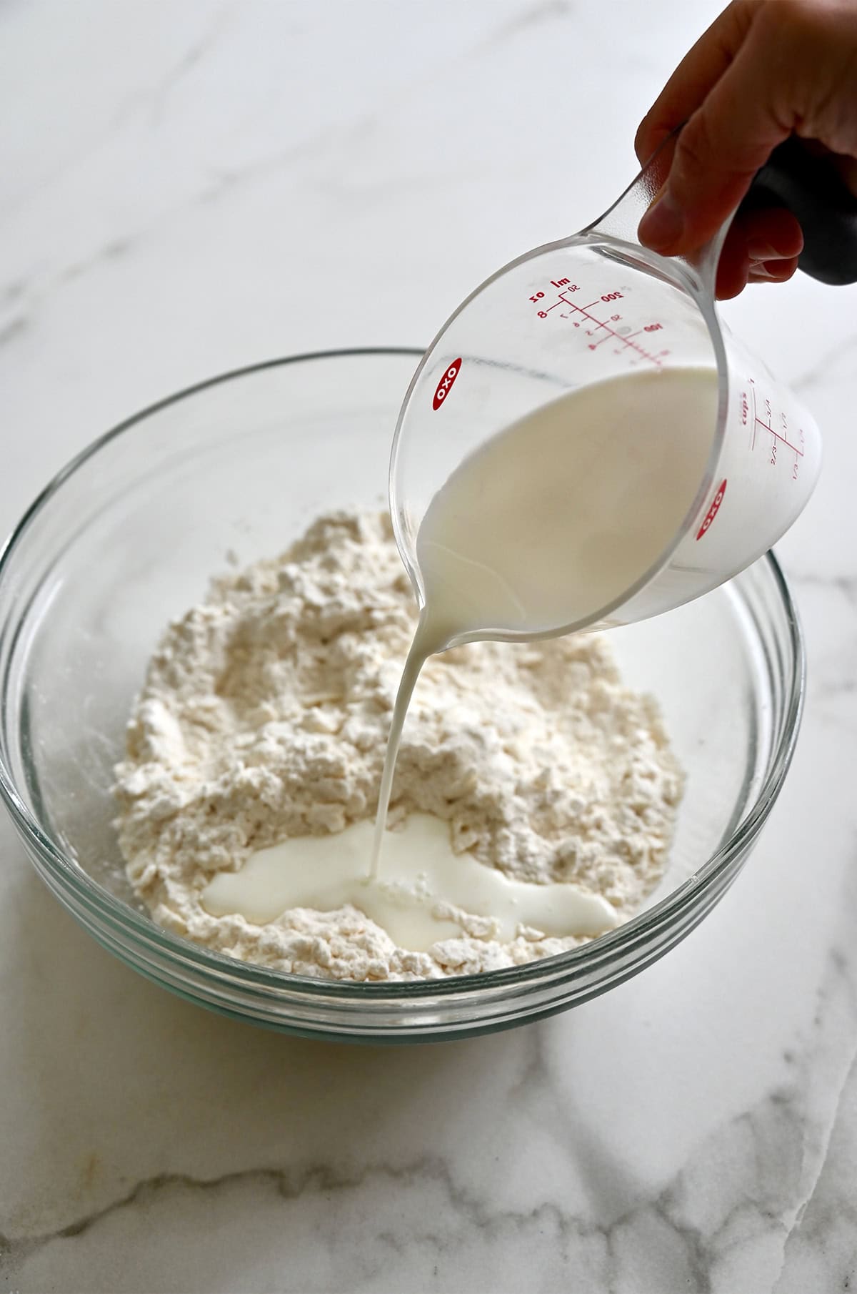 Pouring milk from a liquid measuring cup into a bowl with a flour and butter mixture.