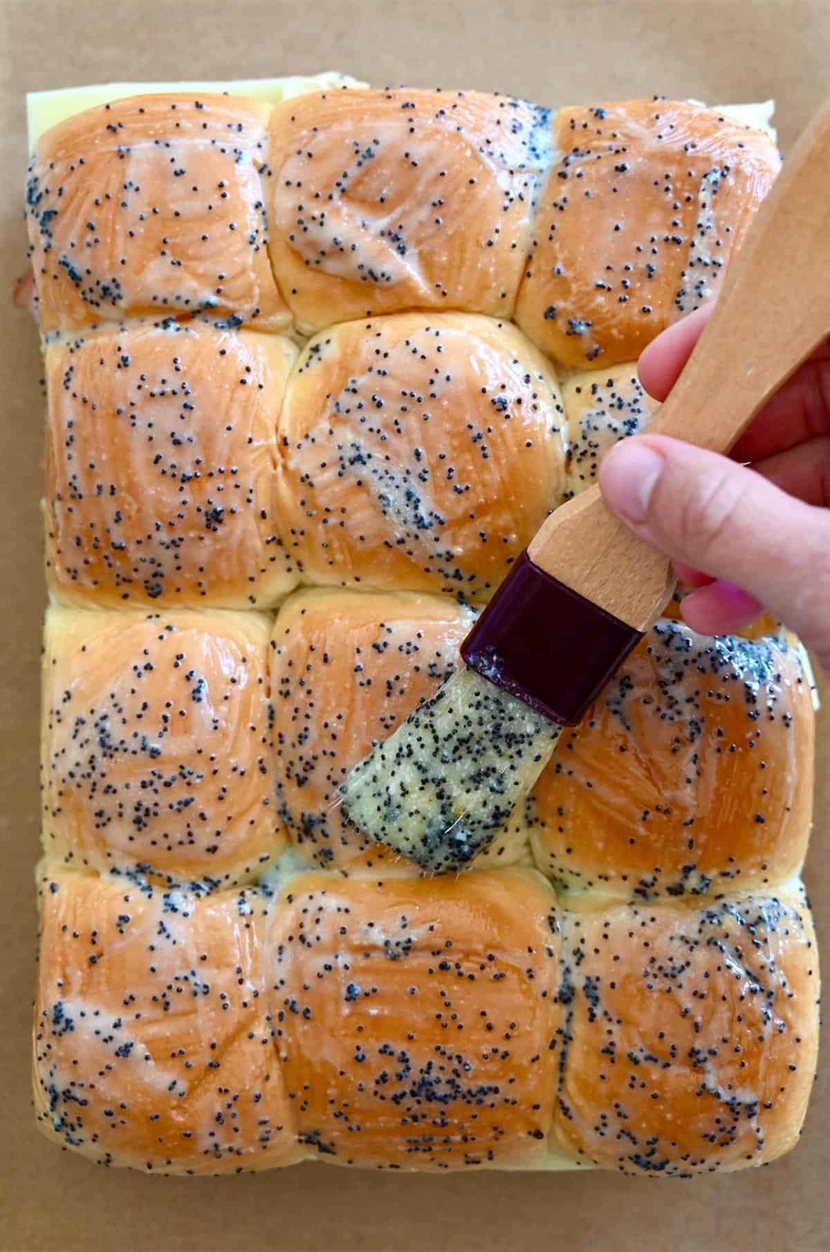 Brushing the tops of sweet slider rolls with poppyseed garlic butter.