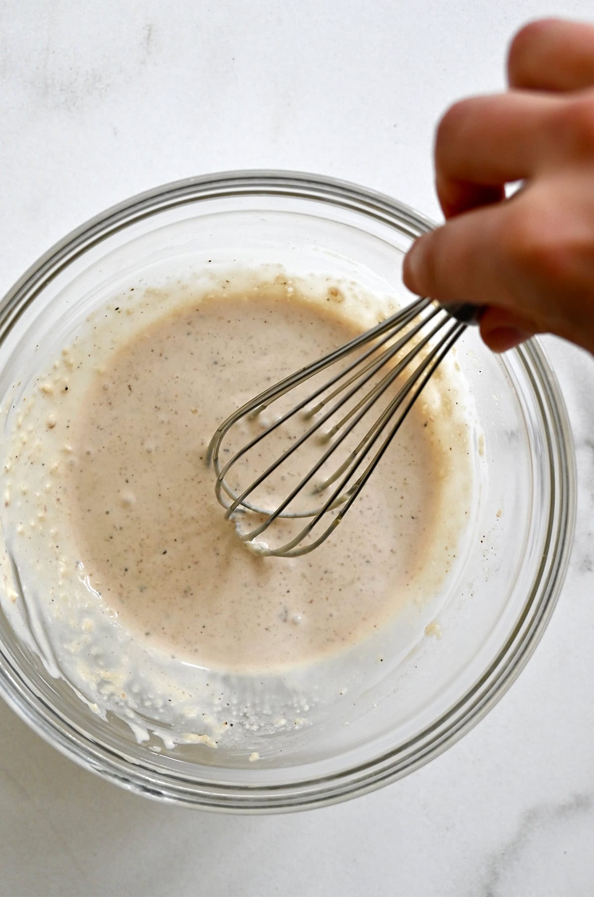 Homemade Caesar salad dressing being whisked together in a bowl.