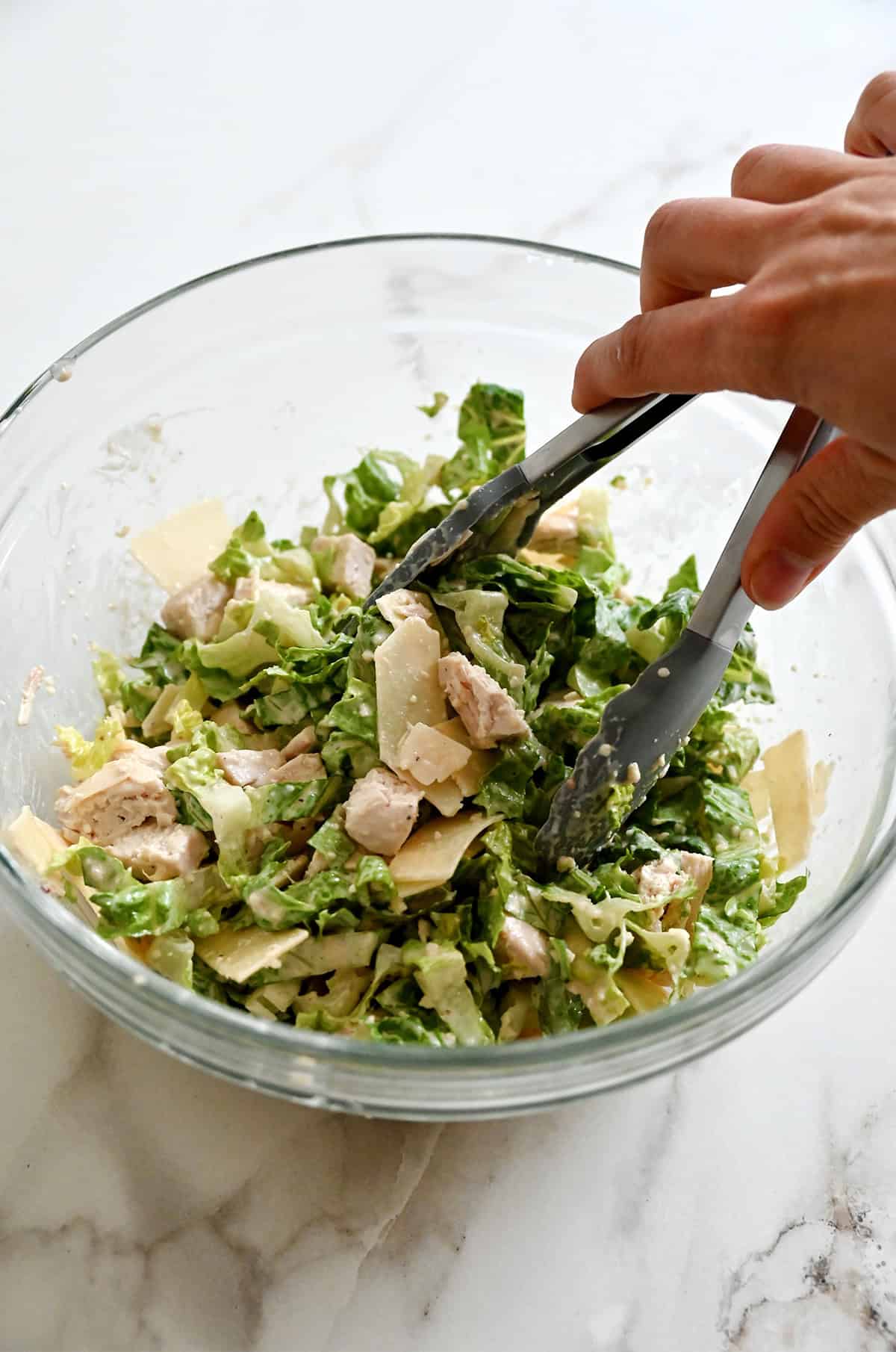 Tossing diced chicken, chopped Romaine, shaved Parmesan and Caesar dressing with tongs in a large bowl.