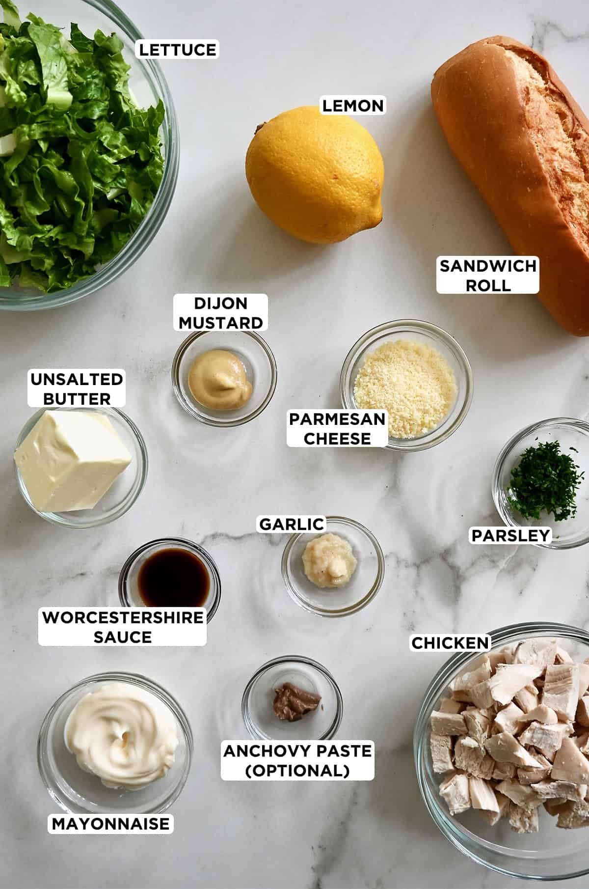 Various sizes of glass bowls containing ingredients to make chicken Caesar salad sandwiches.