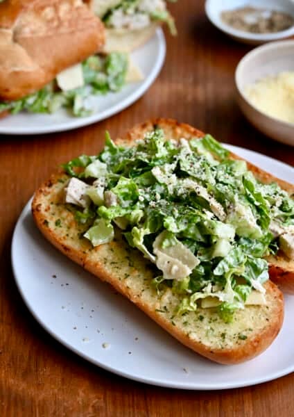 Chicken Caesar sandwich on a toasted hoagie roll with garlic butter on a white plate.