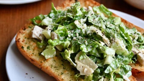Chicken Caesar sandwich on a toasted hoagie roll with garlic butter on a white plate.