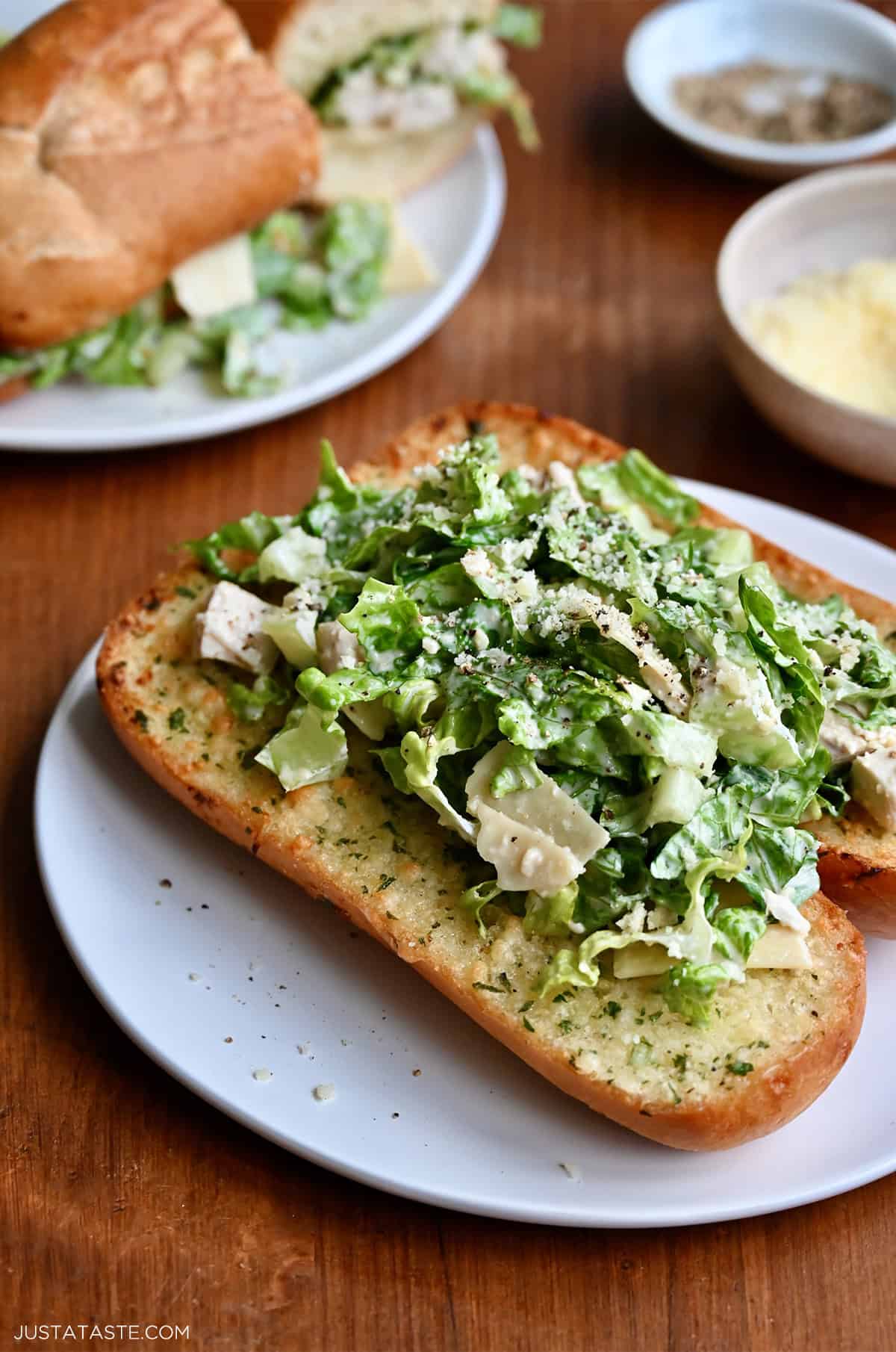Chicken Caesar sandwich on a toasted hoagie roll with garlic butter on a white plate.
