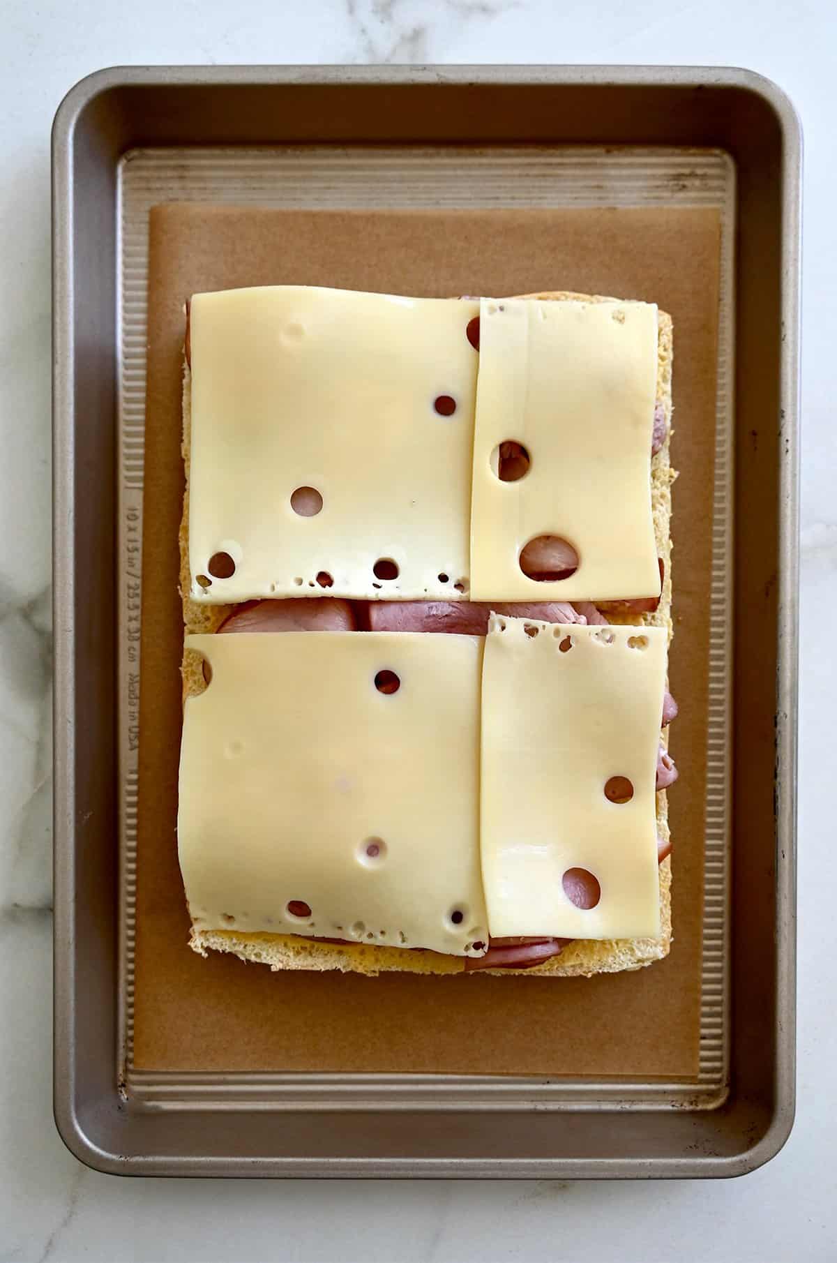 Swiss cheese on top of sliced deli ham on slider rolls.