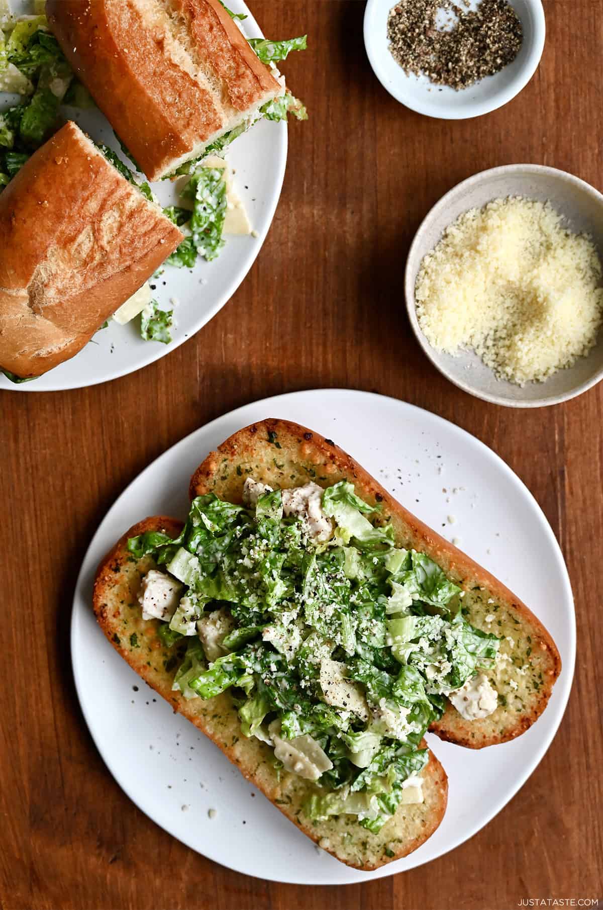 A toasted hoagie laying flat on a plate and topped with chicken Caesar salad and sprinkled with Parmesan cheese.
