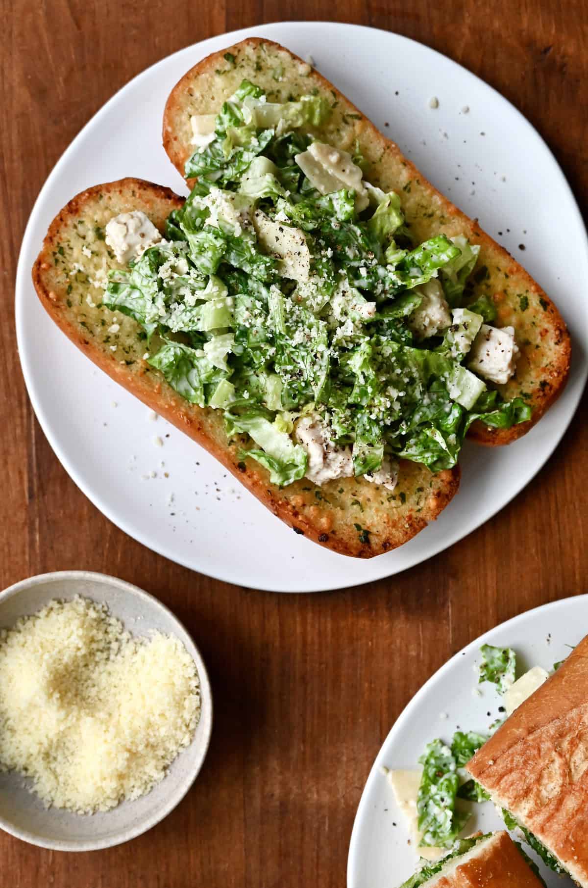 A halved toasted hoagie roll piled high with chopped chicken Caesar salad and plenty of grated Parmesan cheese garnish.