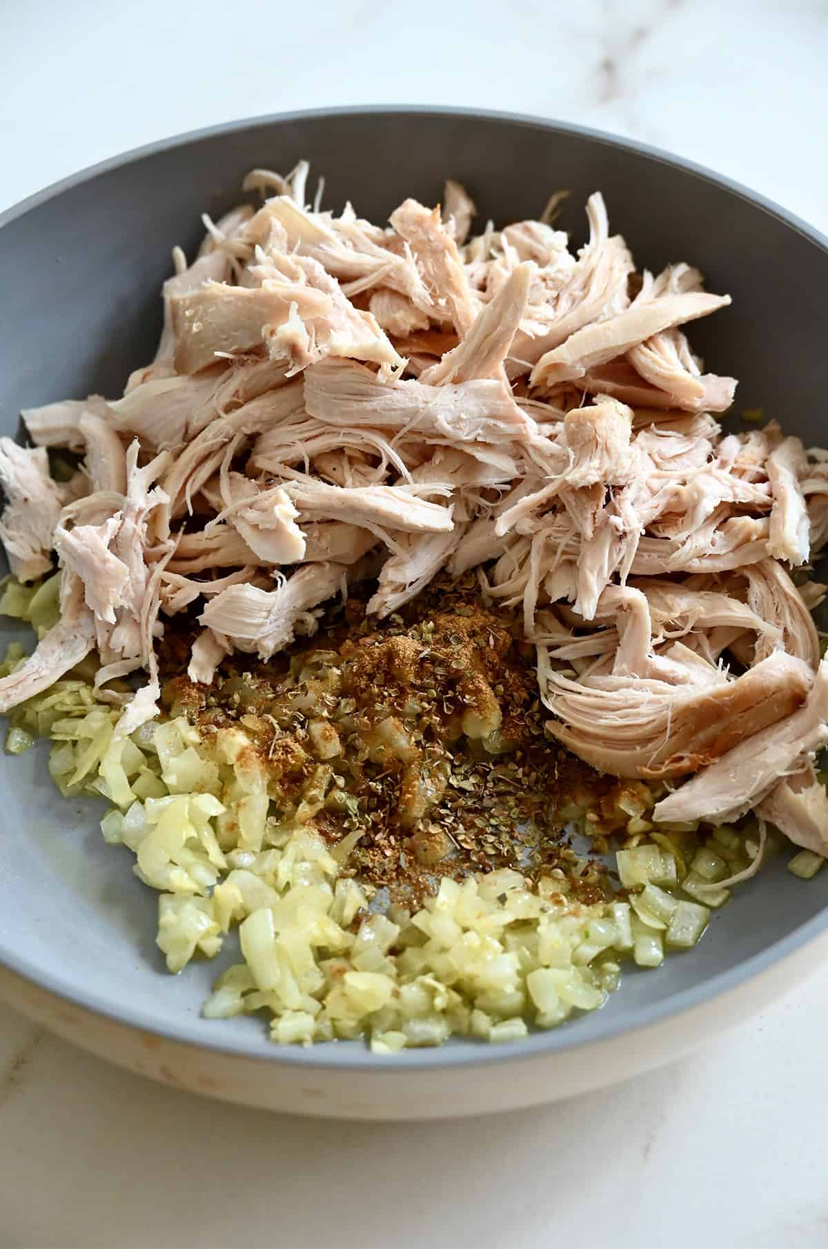 Shredded rotisserie chicken in a skillet with sautéed onions and garlic, cumin and oregano.