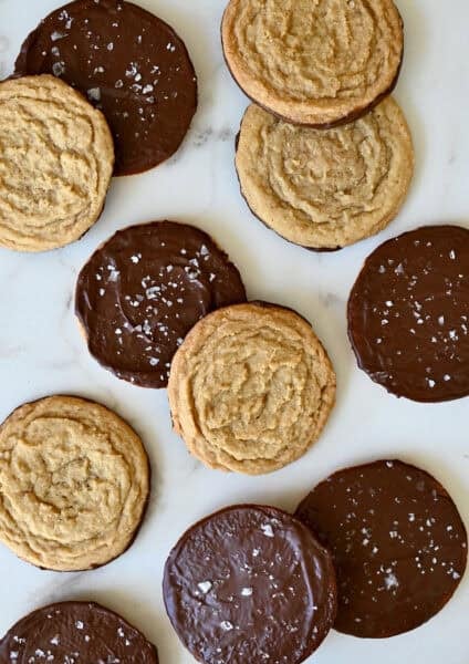 Chocolate chipless cookies, some dipped in chocolate and sprinkled with sea salt, on a marble countertop.
