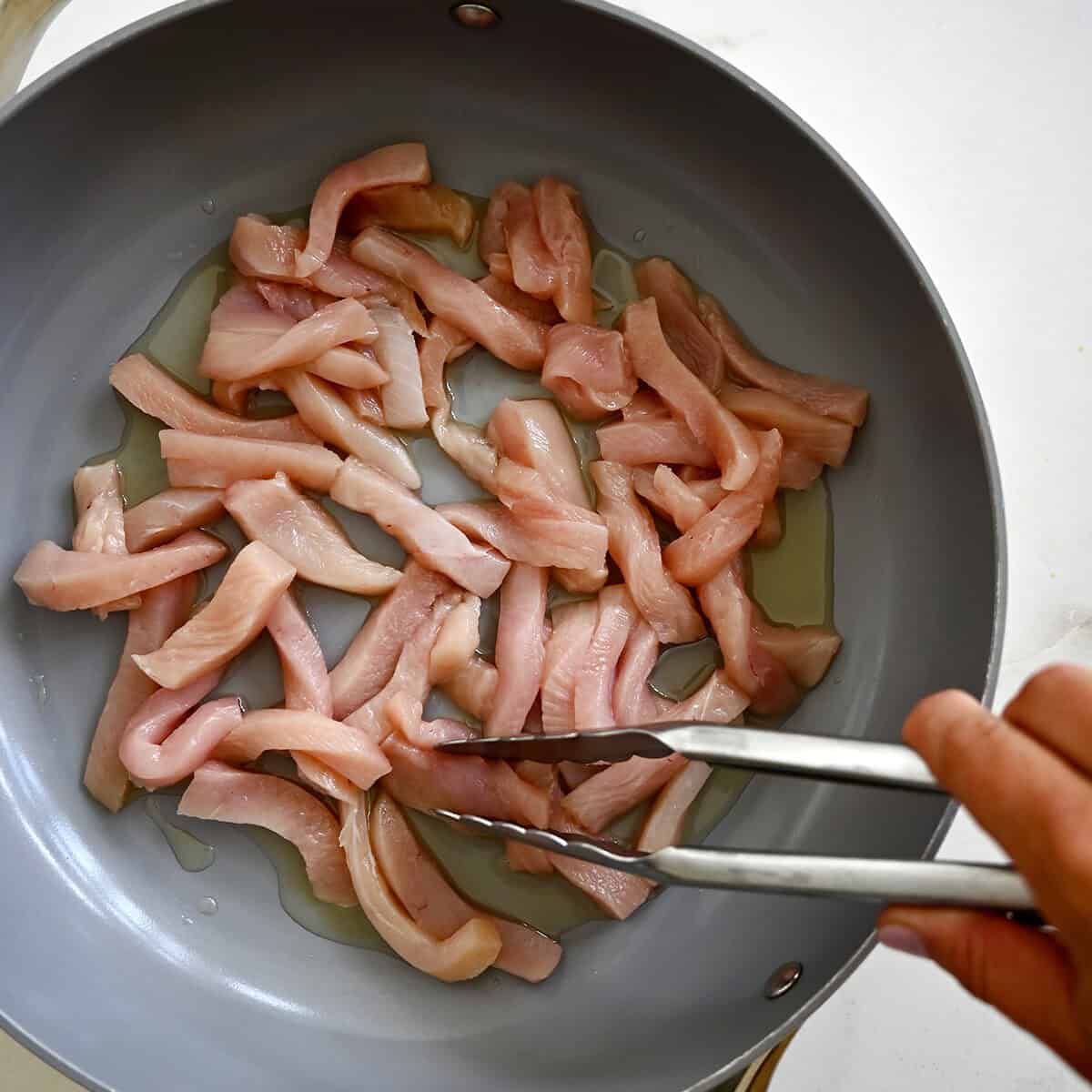 Cooking strips of chicken in a large skillet.