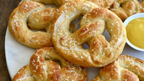 Cottage cheese soft pretzels on a plate with a small ramekin containing yellow mustard.