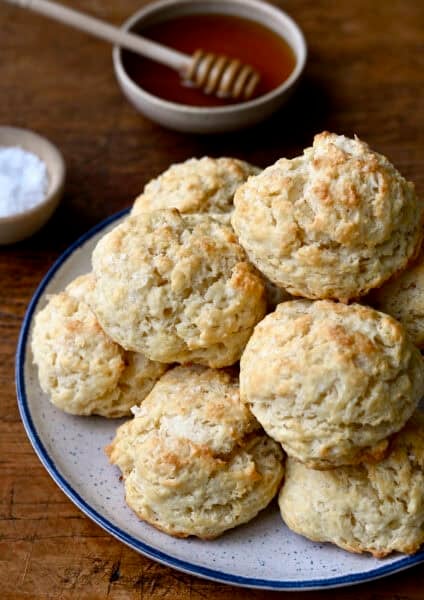 Drop biscuits piled high on a plate with a small bowl containing honey nearby.