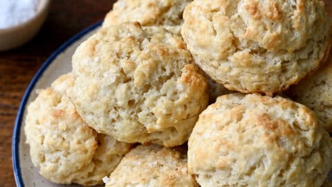 Drop biscuits piled high on a plate with a small bowl containing honey nearby.