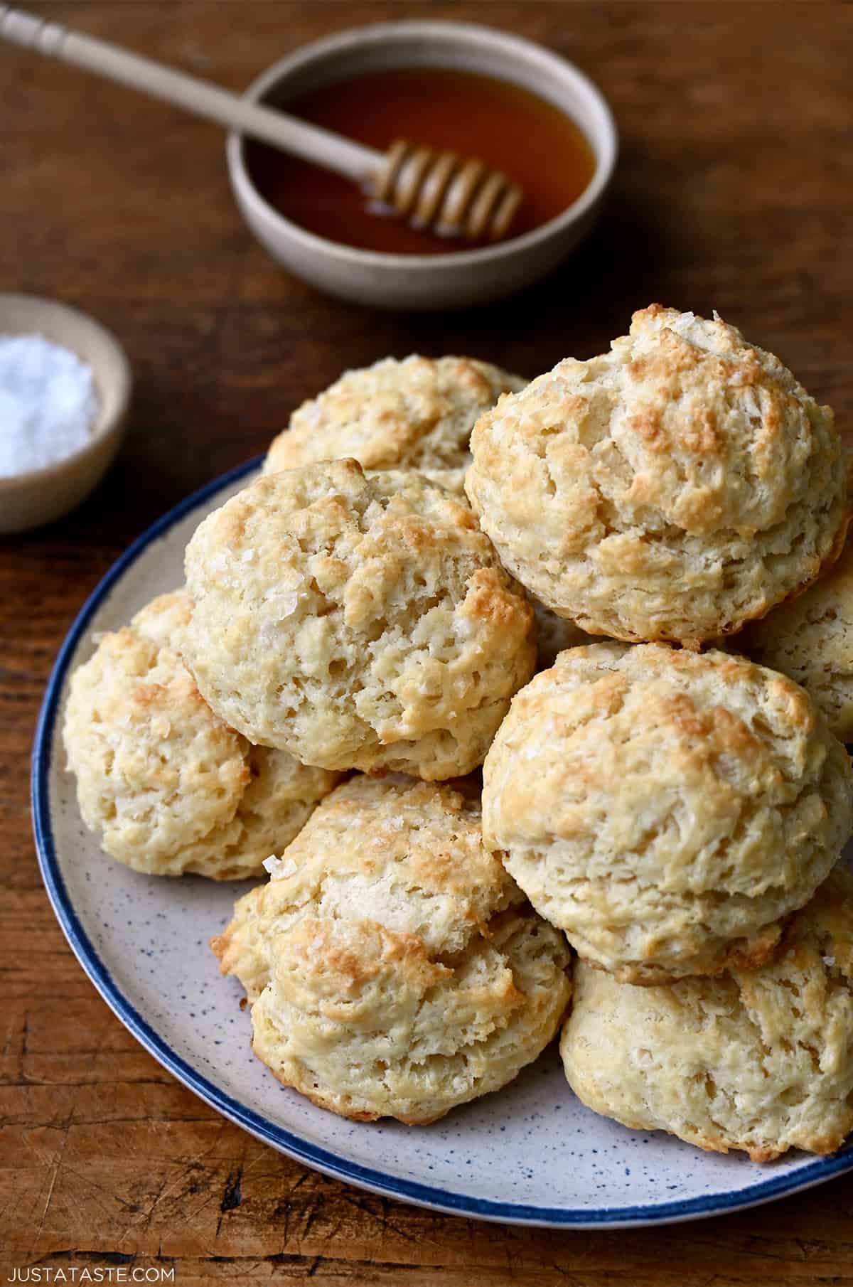 Drop biscuits piled high on a plate with a small bowl containing honey nearby.