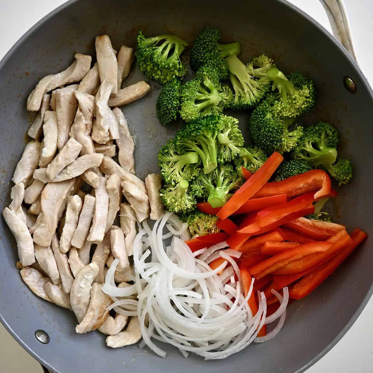 Cooked chicken, red bell peppers, sliced onion and broccoli florets in a large skillet.
