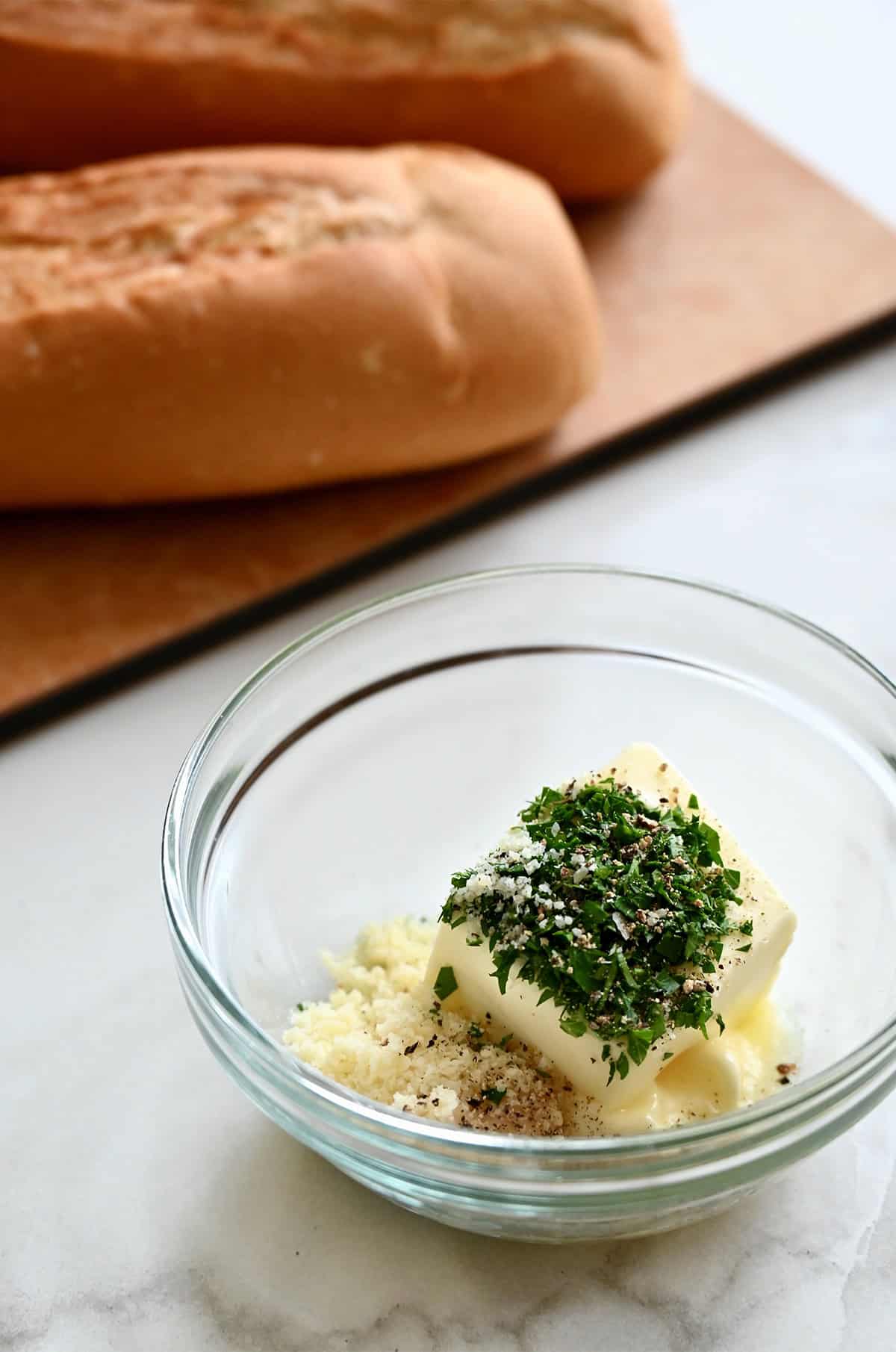 A small bowl containing butter, minced parsley, grated Parmesan and minced garlic.