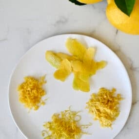 A plate with lemon zest that shows zest from four different techniques: A citrus zester, a microplane, a box grater and a vegetable peeler.