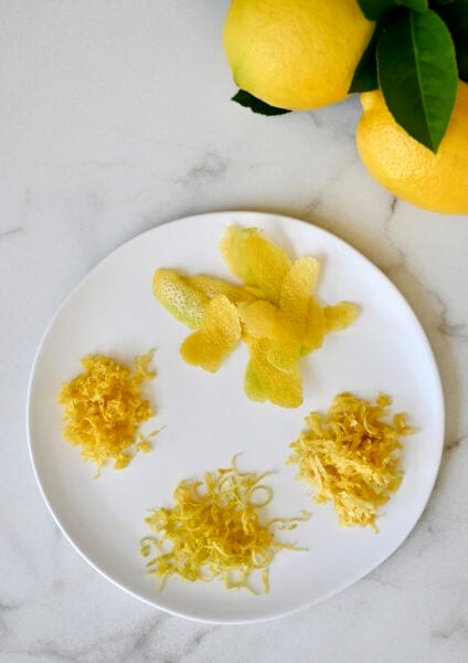 A plate with lemon zest that shows zest from four different techniques: A citrus zester, a microplane, a box grater and a vegetable peeler.