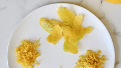 A plate with lemon zest that shows zest from four different techniques: A citrus zester, a microplane, a box grater and a vegetable peeler.