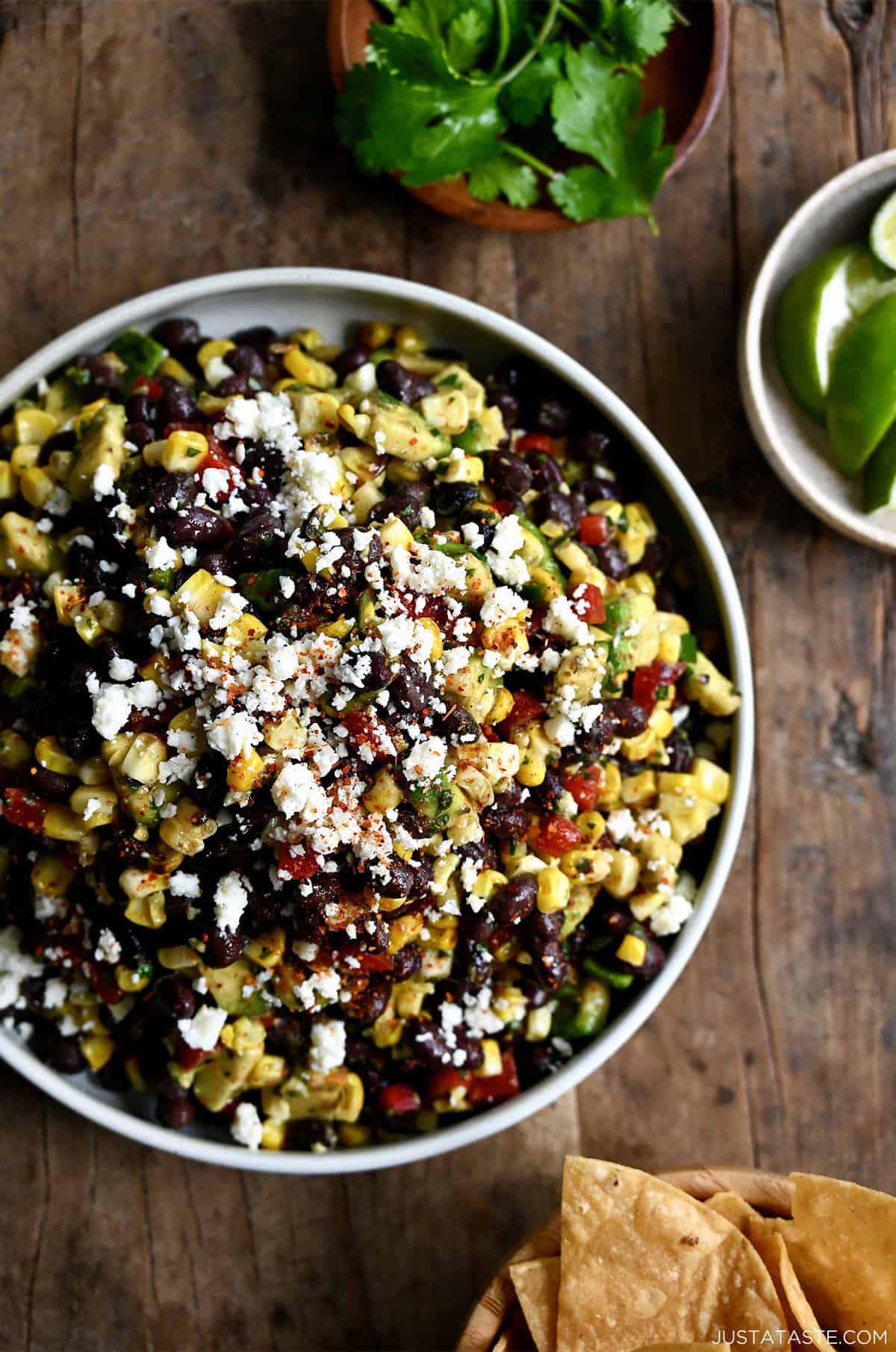 A serving bowl containing black bean and corn salad garnished with Cojita cheese. A bowl of tortilla chips is nearby.