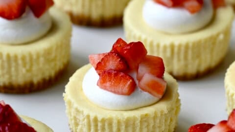 Mini cottage cheese cheesecakes topped with a dollop of whipped cream and chopped fresh strawberries on a serving plate.