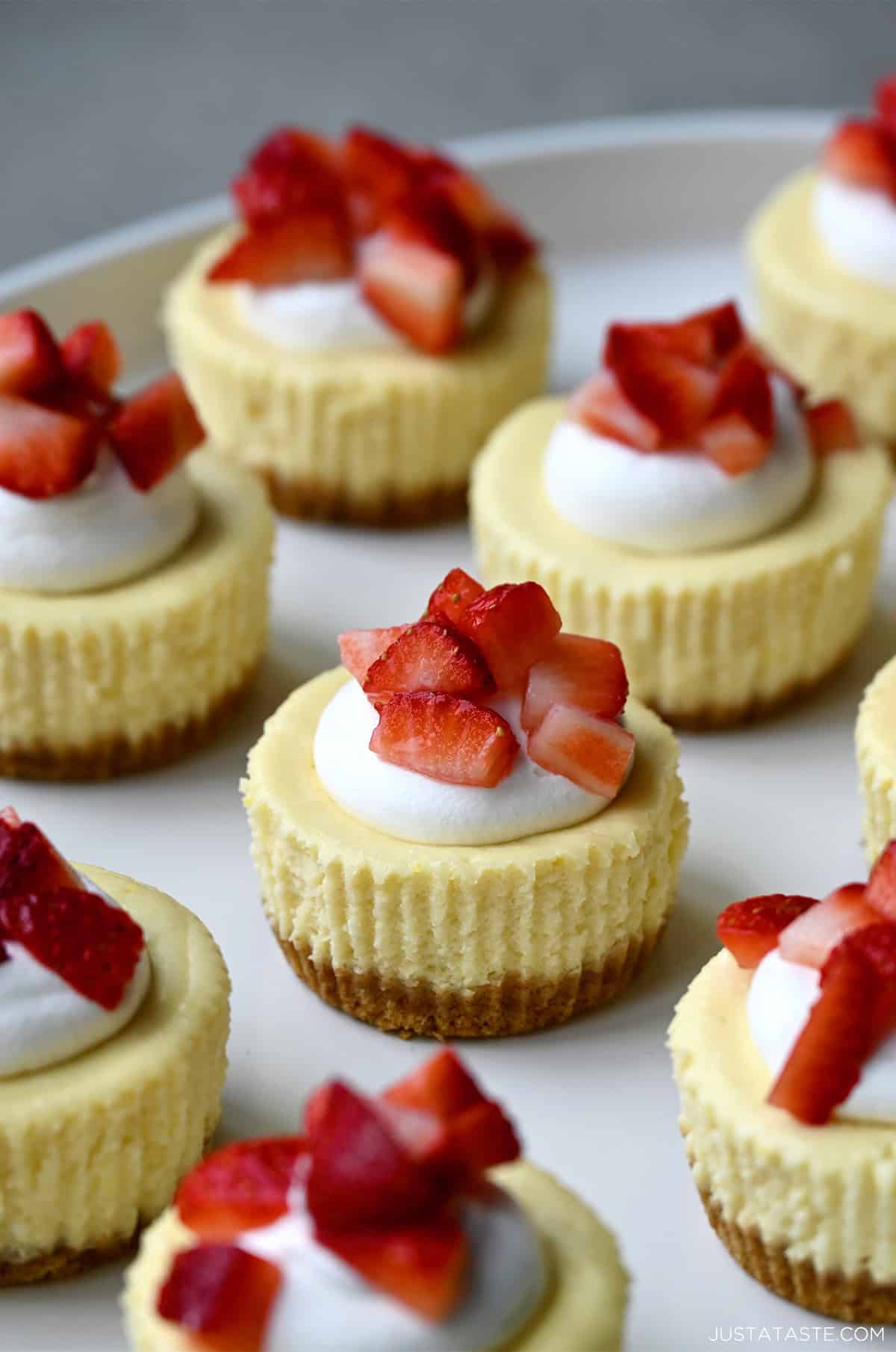 Mini cottage cheese cheesecakes topped with a dollop of whipped cream and chopped fresh strawberries on a serving plate.