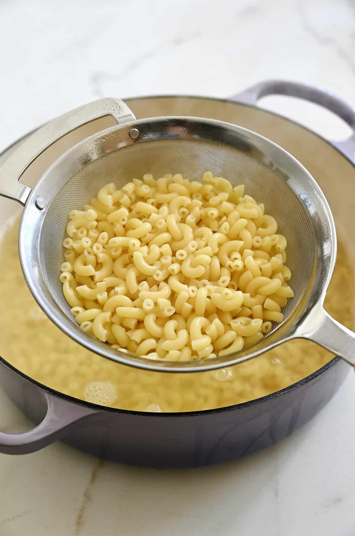 Al dente elbow pasta in a mesh strainer over a pot of salted water.