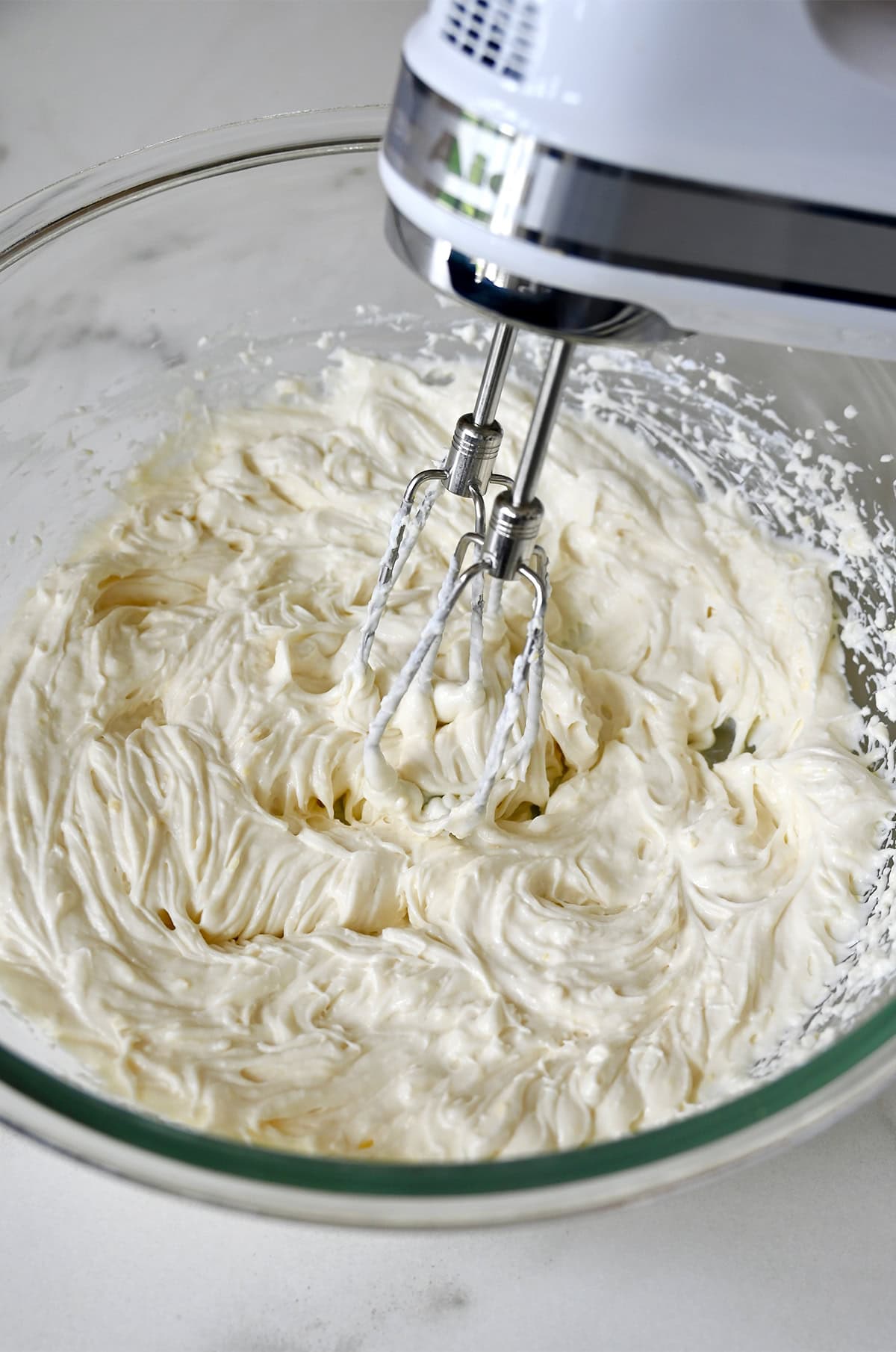 Silky smooth cheesecake mixer in a bowl with a handheld electric mixer.