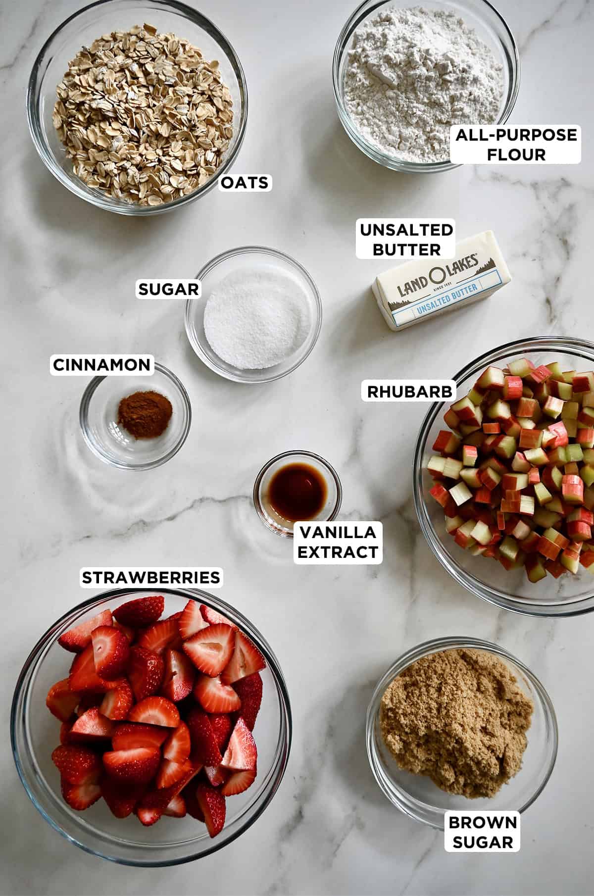 Various sizes of glass bowls containing ingredients to make strawberry rhubarb crisp.