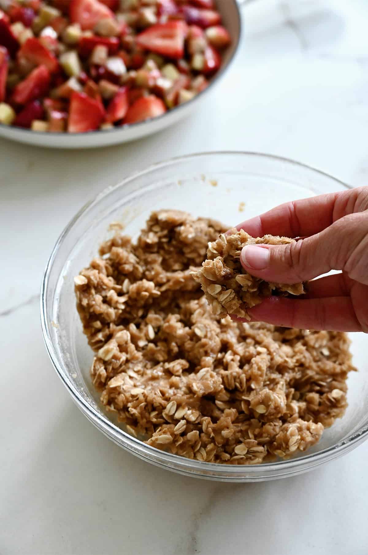 A hand clumps together crisp topping in a small bowl.