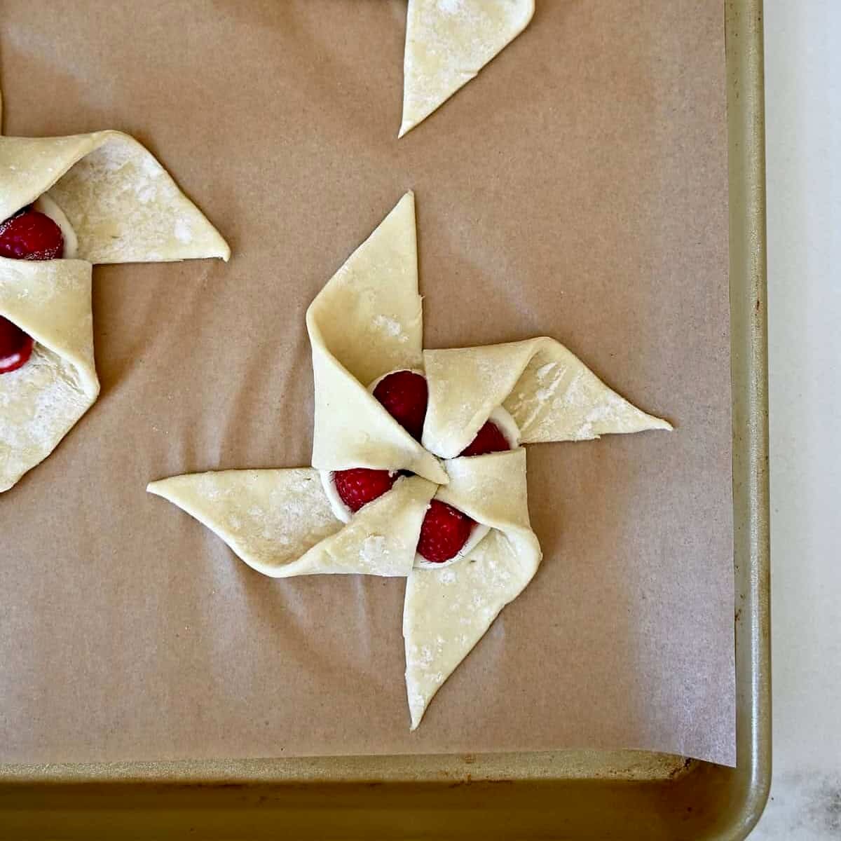 Step 4 in shaping a pinwheel puff pastry: Folding the final corner into the center.