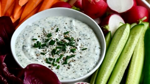 Cottage cheese dip in a bowl on a platter surrounded by fresh carrots, radishes, cucumbers and cherry tomatoes.