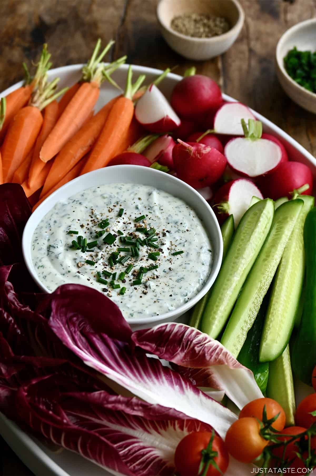 Cottage cheese dip in a bowl on a platter surrounded by fresh carrots, radishes, cucumbers and cherry tomatoes.