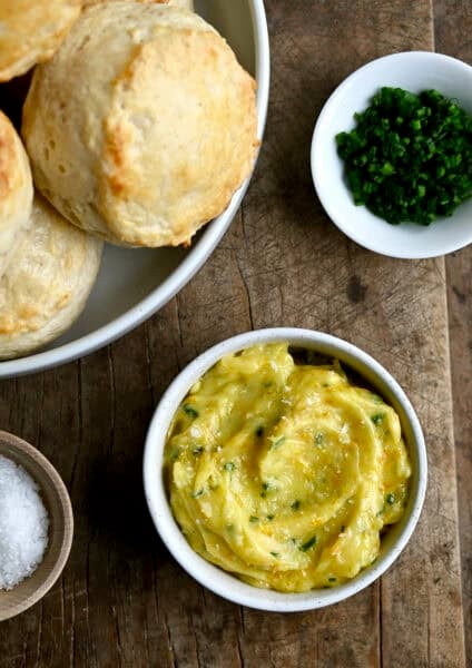 Homemade honey butter in a small bowl next to a bowl piled high with flaky buttermilk biscuits.