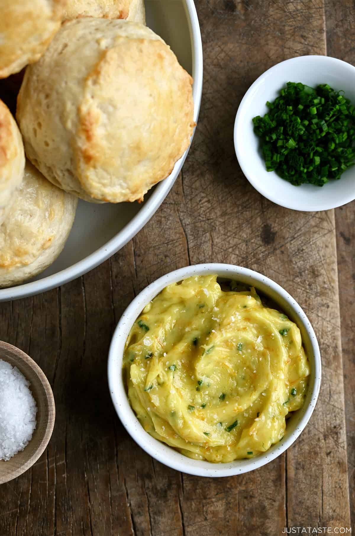 Homemade honey butter in a small bowl next to a bowl piled high with flaky buttermilk biscuits.