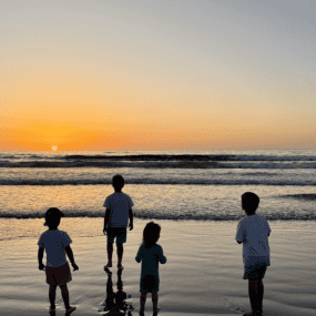 Four kids standing on the beach watching the sunset.