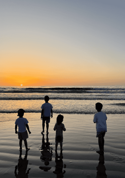 Four kids standing on the beach watching the sunset.