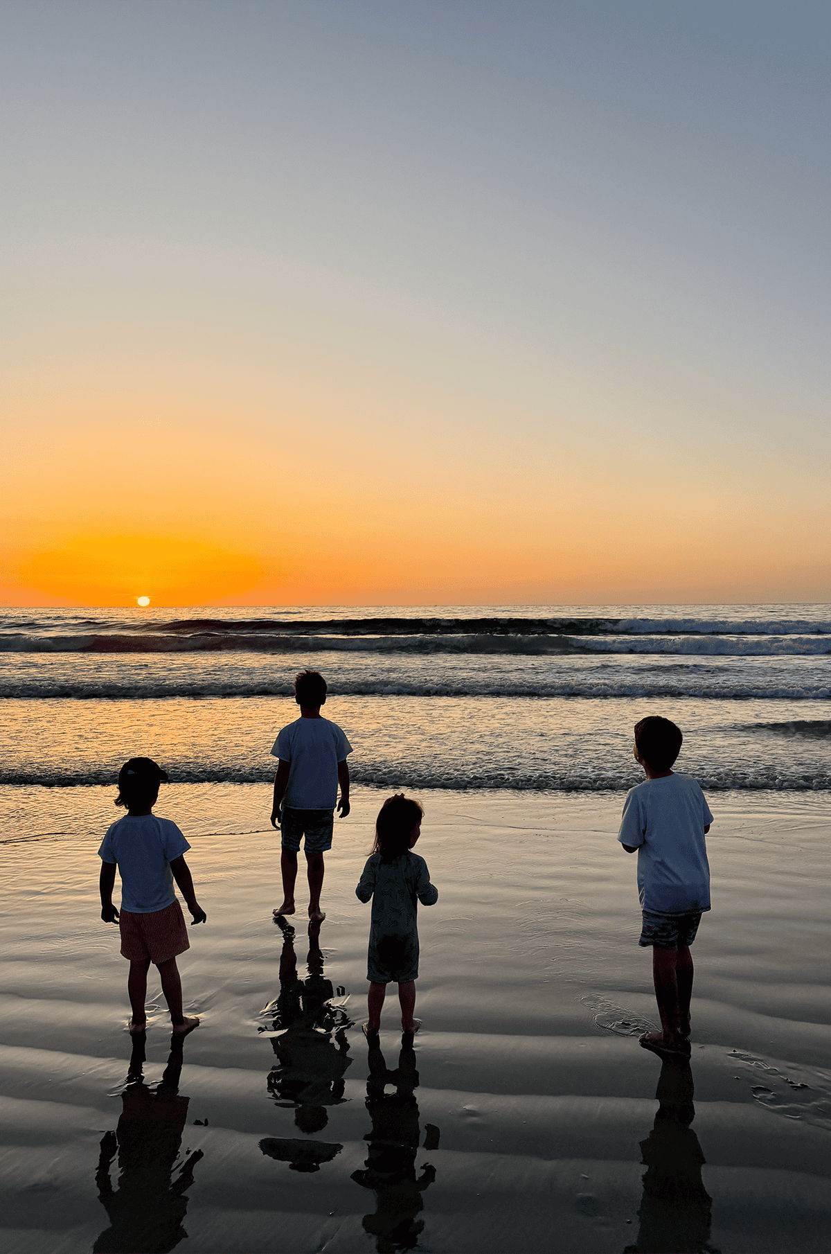 Four kids standing on the beach watching the sunset.
