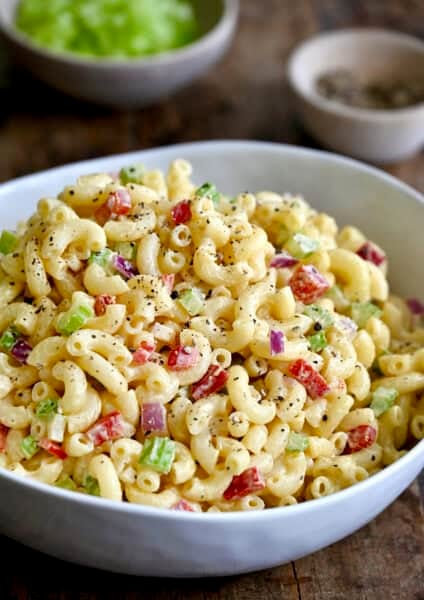 A serving bowl containing macaroni salad with diced red onion, diced celery and diced red bell pepper, all tossed in a creamy homemade dressing.