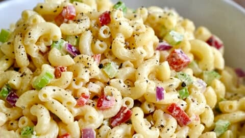 A serving bowl containing macaroni salad with diced red onion, diced celery and diced red bell pepper, all tossed in a creamy homemade dressing.