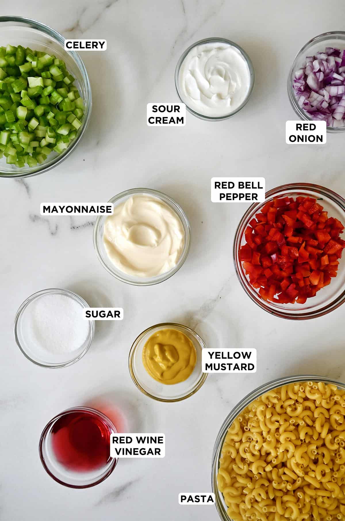 Ingredients to make macaroni salad in various sizes of glass bowls.