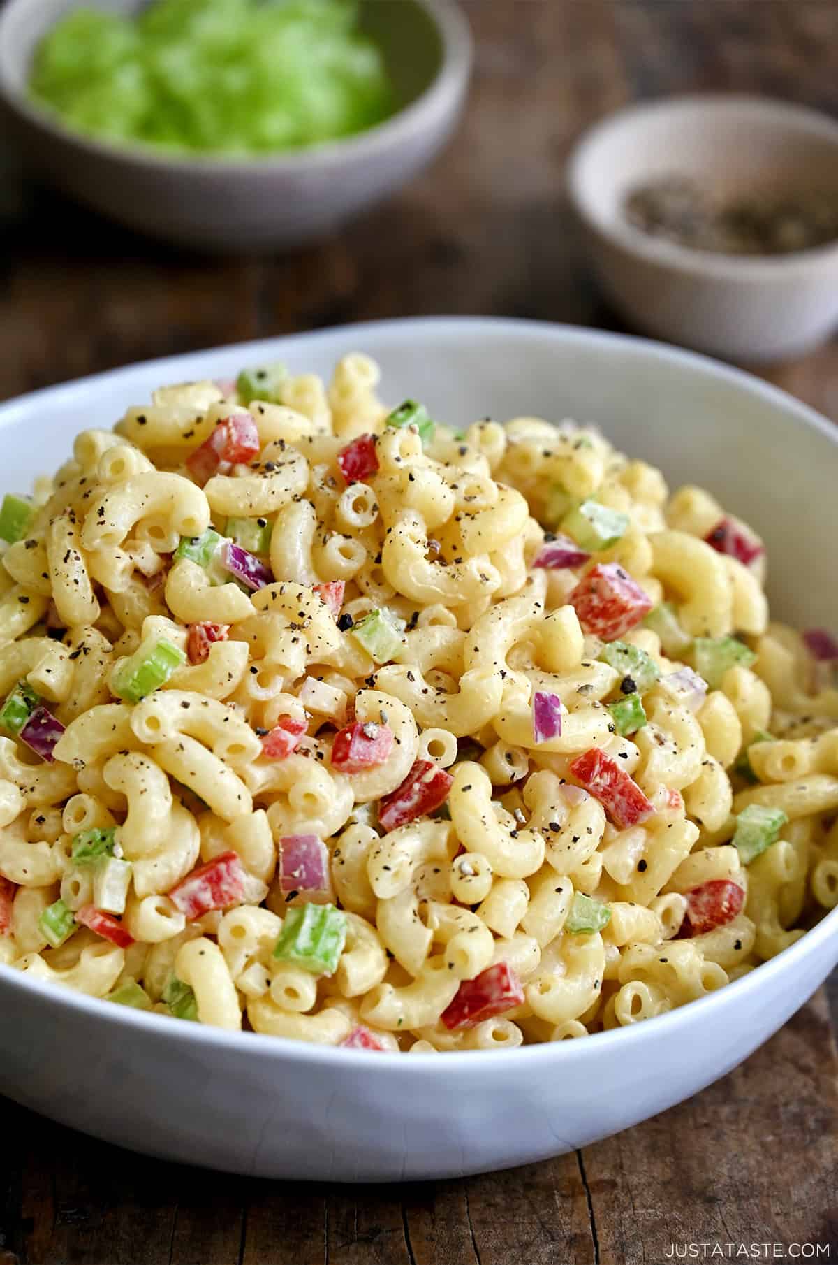 A serving bowl containing macaroni salad with diced red onion, diced celery and diced red bell pepper, all tossed in a creamy homemade dressing.