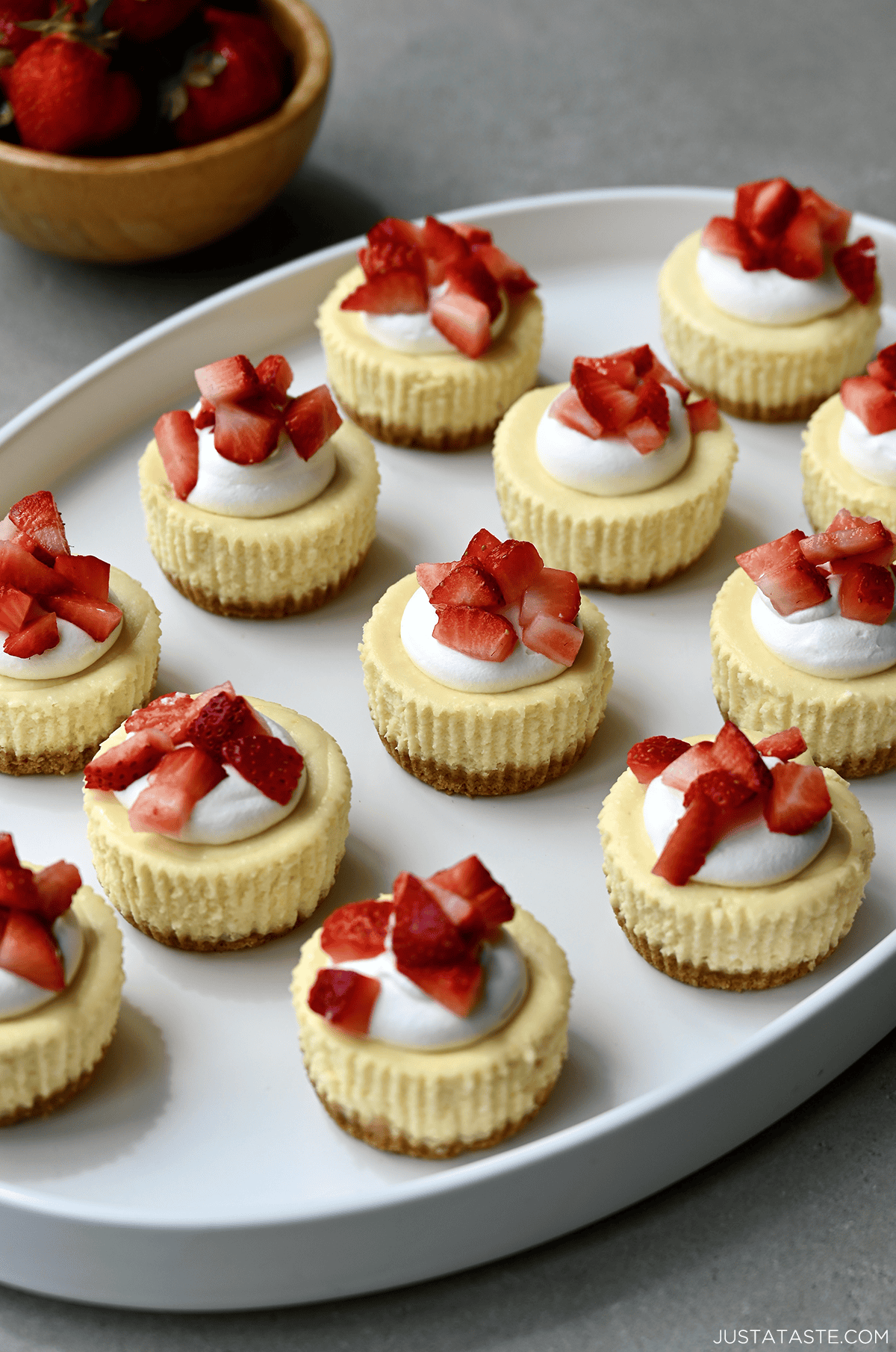 Cottage cheese cheesecake cups topped with whipped cream and diced strawberries on a white serving tray.