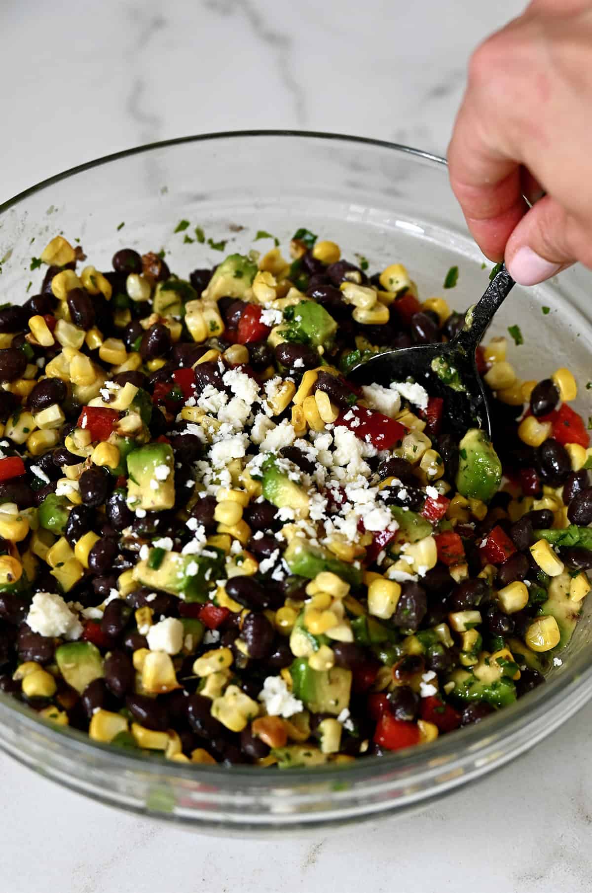 Avocado, black bean and corn salad all tossed in a honey lime dressing and topped with Cojita cheese in a glass mixing bowl.