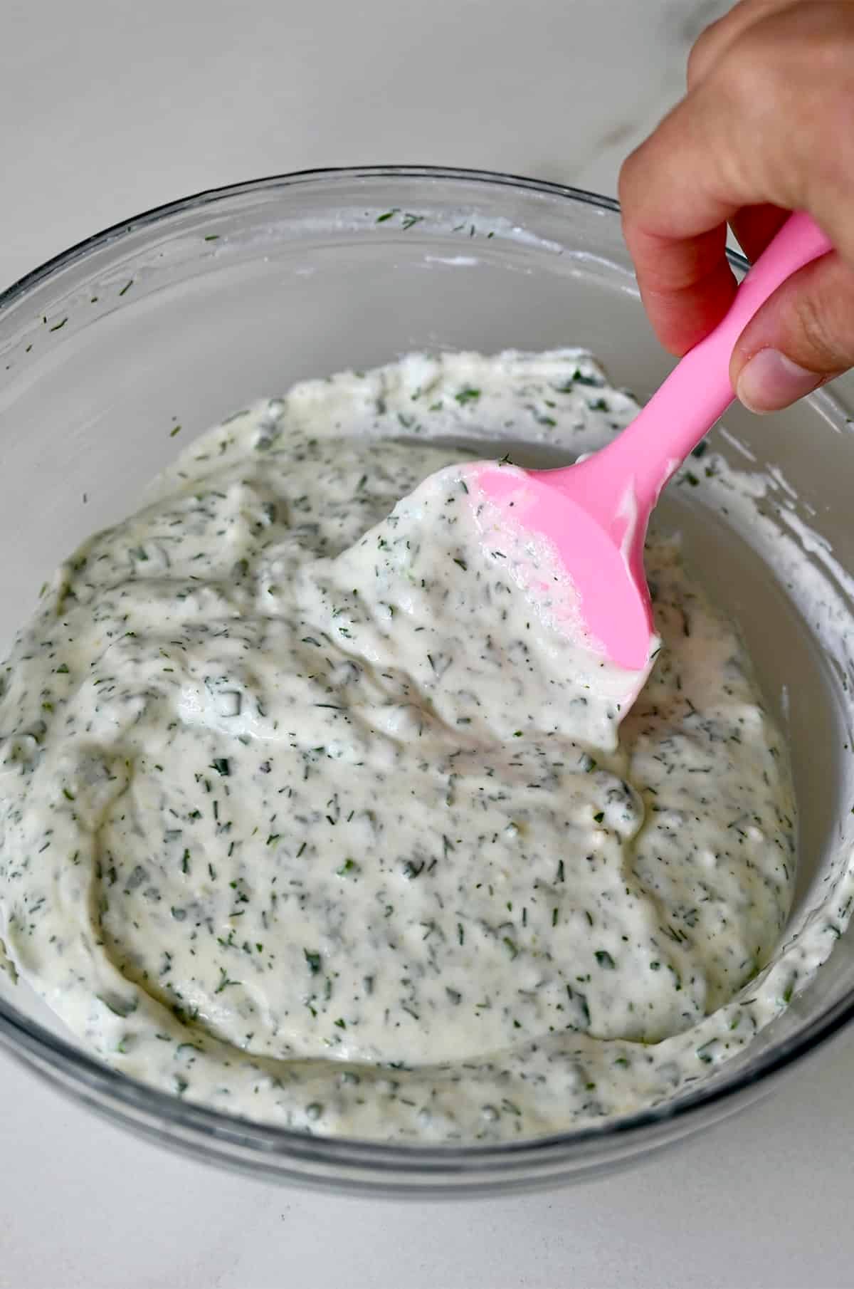 Cottage cheese dip with herbs and spices in a bowl with a pink spatula.