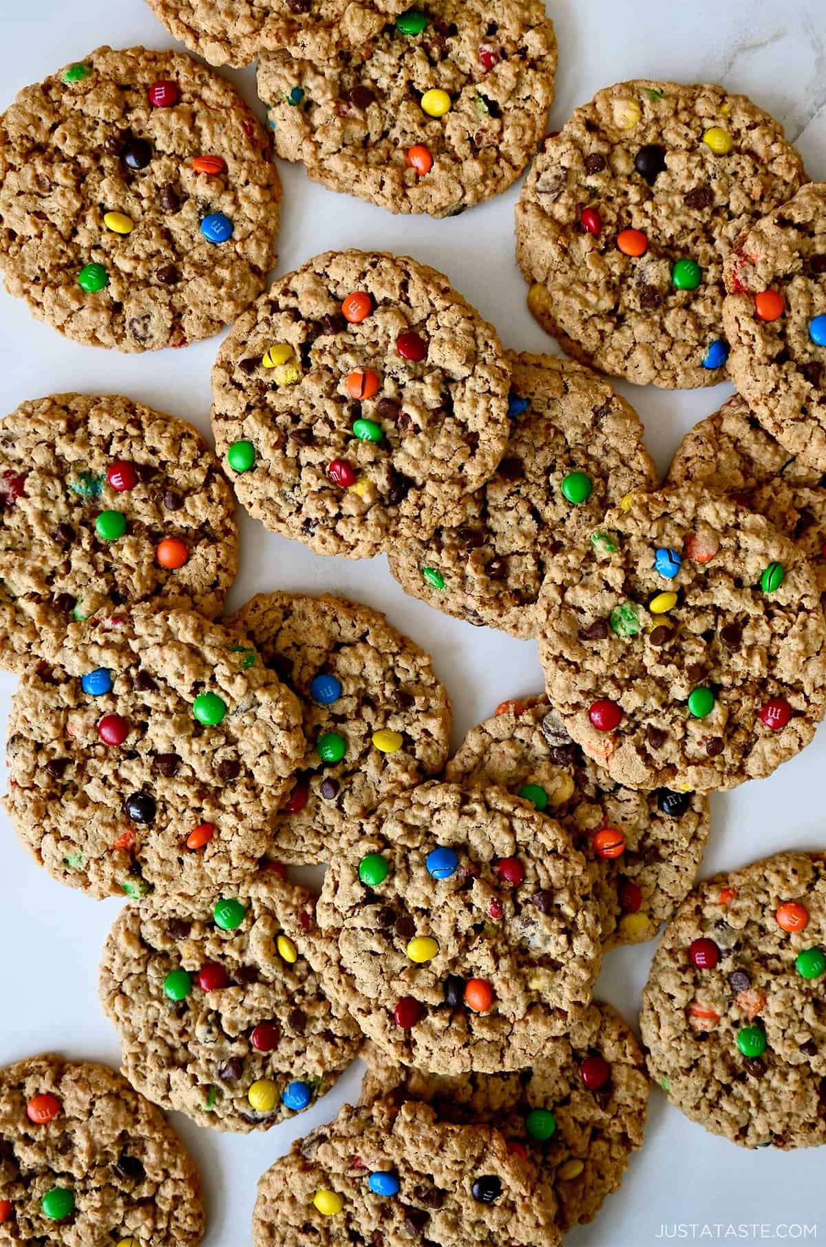 Monster cookies studded with M&Ms and chocolate chips piled atop each other on a marble surface.