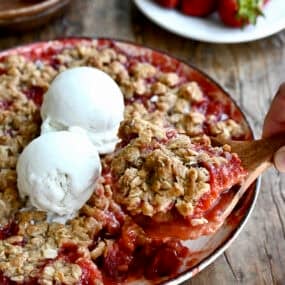 Strawberry rhubarb crisp in a baking dish, topped with two scoops of vanilla ice cream.
