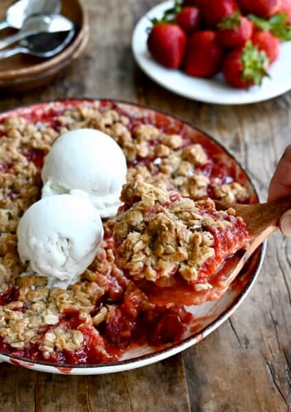 Strawberry rhubarb crisp in a baking dish, topped with two scoops of vanilla ice cream.