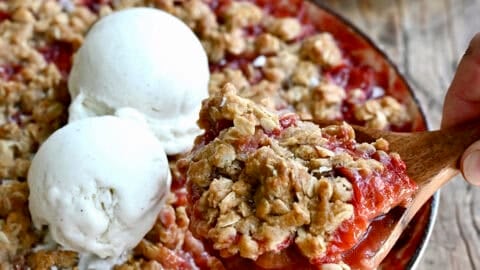Strawberry rhubarb crisp in a baking dish, topped with two scoops of vanilla ice cream.